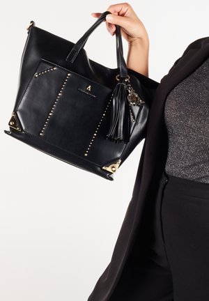 Sort læder tote bag med guldfarvet hardware, naglet design og en frynseaccent. Den har en rummelig indvendig plads og en struktureret form.