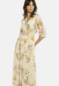 Pikk lilleline kleit heledas kollases toonis. Omadusteks on õhulised varrukad, V-kaelus, vöökohal rihm ja voolav siluett. Muster sisaldab pastelseid lilli.