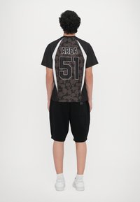 Camisola atlética preta com as costas estampadas apresentando o texto "AREA 51", combinada com calções pretos e ténis brancos.