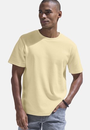 Yellow textured short-sleeve t-shirt with a round neckline, featuring a loose fit and subtle grid pattern, paired with light grey jeans.