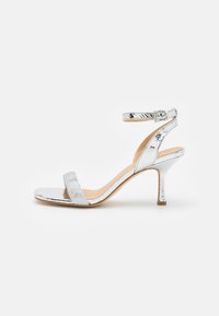 Sandalie argintii cu toc înalt, cu un model texturat de reptilă, curea pentru glezna și un toc subțire stiletto, prezentând un design elegant și minimalist.