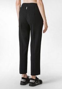 Schwarze Hose mit elastischem Bund, flacher Vorderseite, schmal zulaufenden Beinen und Umschlägen, kombiniert mit schwarzen Sneakers mit kontrastierenden Markenakzenten.