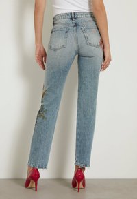 Jeans de mezclilla azul claro con bordado floral en los muslos, diseño de pierna recta, dobladillo deshilachado y un bolsillo trasero con sutil branding.