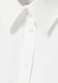Gros plan sur une chemise blanche à col avec trois boutons translucides visibles, attachés le long de la patte de boutonnage avant.