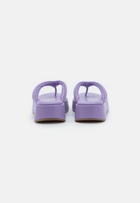 Lavender-padded platåsandaler med thong-remmar som visas bakifrån på en vit bakgrund.