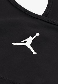 Material sport negru cu logo Jumpman alb, cu textură netedă și design simplu. Guler rotund cu margini cusute.