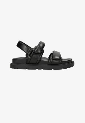 Sandales en cuir noir avec des sangles ajustables, une semelle plate durable et un design minimaliste. Présente des accents de couture et un détail de logo.
