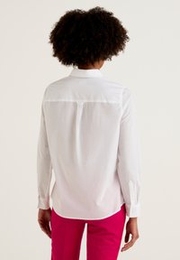 Camisa blanca de botón con mangas largas, que presenta un yugo trasero y un brillo sutil, combinada con pantalones rosa brillante.