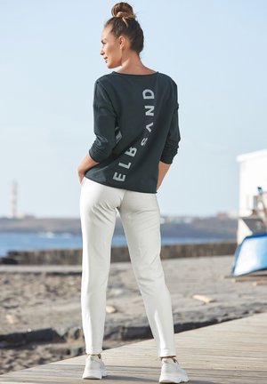 Dark gray long-sleeve shirt with the word "ELBSAND" printed vertically on the back, paired with white fitted pants and white sneakers.