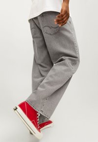 Jeans grigi ampi in un tessuto denimb leggero presentano un classico design a cinque tasche. Abbinati a sneakers rosse alte.