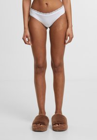 White cotton panties with a lace trim at the waistband, paired with brown fluffy slippers featuring an open toe design.