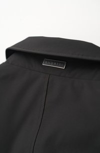 Schwarze Jacke mit glatter Textur, spitzem Kragen und rechteckigem silbernem Etikett mit dem eingeprägten Markennamen "bugatti".