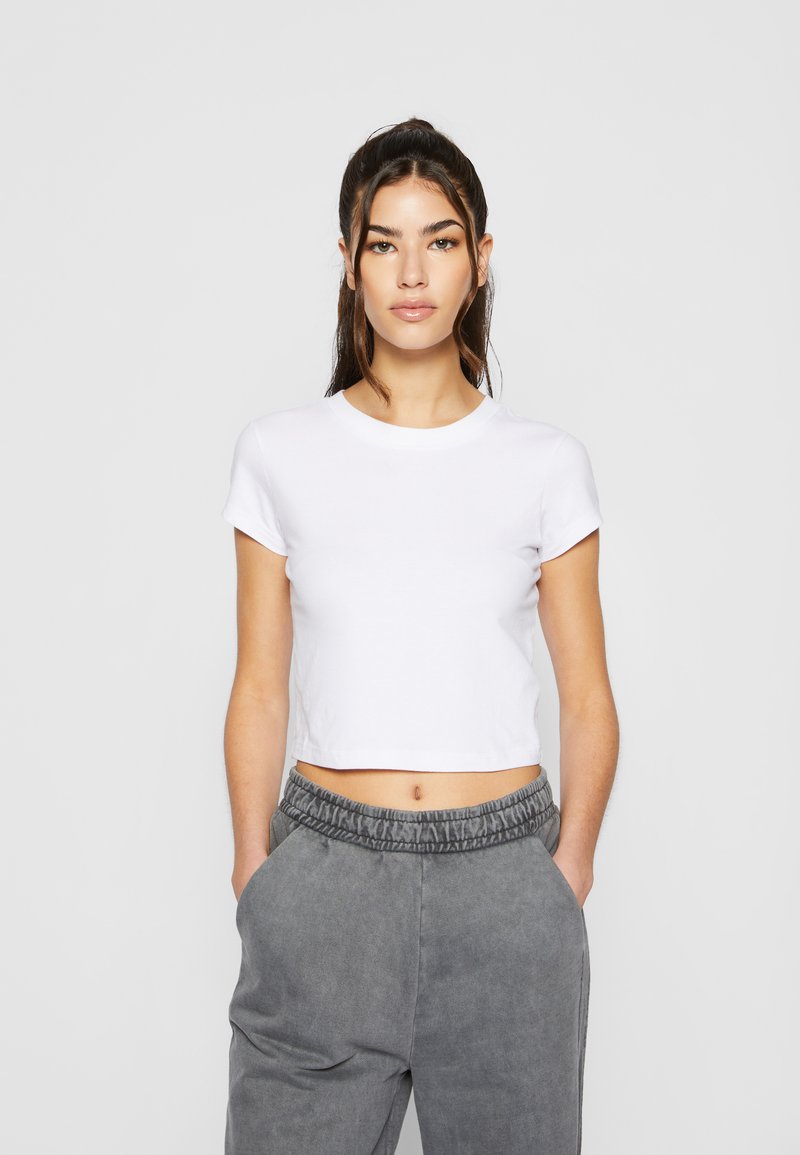 Weißes, kurzes T-Shirt mit runder Ausschnitt und kurzen Ärmeln, kombiniert mit grauen, hochgereihten Hosen mit elastischem Bund und Seitentaschen.