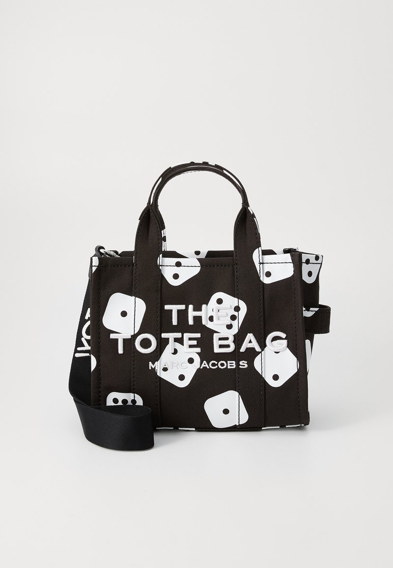Crna torba s uzorkom bijelih kockica, čvrsti ručki, podesiva ramena traka, i istaknuti bijeli tekst koji kaže "TORBA MARC JACOBS."