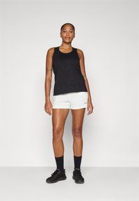 Canotta nera con motivo testurizzato, pantaloni corti bianchi, scarpe nere e calzini neri. Design minimalista senza loghi visibili, posizione in piedi.