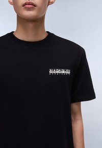 Tricou negru din bumbac cu guler rotund, având un logo de marcă imprimat în alb în zona pieptului stâng. Mâneci scurte, textură netedă.