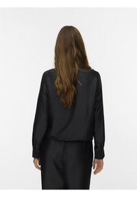 Schwarze, kurz geschnittene Bluse mit langen Ärmeln und glatter Textur. Verfügt über geknöpfte Manschetten und einen taillierten Saum, von hinten dargestellt.