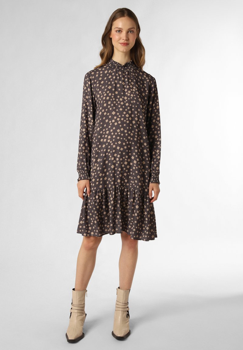 Langärmliges Kleid aus dunkelgrauem Stoff mit hellbeigen quadratischen Mustern, gerafftem Kragen und gestuftem Volant-Saum. Kombiniert mit beigen Ballerinas.