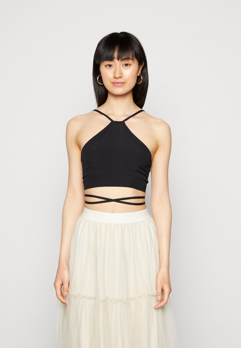 Top cropped preto com alças finas e um design cruzado na cintura, combinado com uma saia leve de tule em camadas.