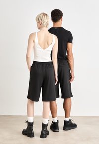 Shorts de sport noirs avec taille élastique, associés à un débardeur blanc texturé. Sujet à des bottines tendance et des chaussettes de longueur mi-mollet.