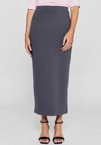 Grijze lange rok van zacht, rekbaar materiaal. Beschikt over een slimfit tailleband en een rechte snit, gecombineerd met zwarte sandalen met banden.