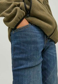 Fleecejacka i olivgrön med dragkedja i kragen, kombinerad med blå denimjeans med en klassisk femficksdesign och synlig sömnad.