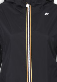 Giacca nera con cappuccio, dotata di una zip bianca e strisce verticali multicolori (rosse, gialle e verdi) lungo la zip.