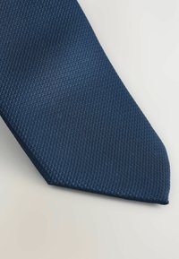 Marineblå slips med et struktureret, vævet mønster, der har en spids ende. Stoffet ser glat ud med en let glans.