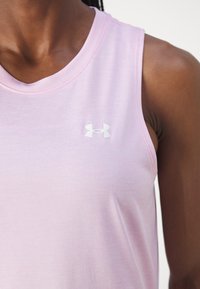 Närbild av en person som bär en ärmlös rosa träningsöverdel med en vit Under Armour-logotyp på bröstet.