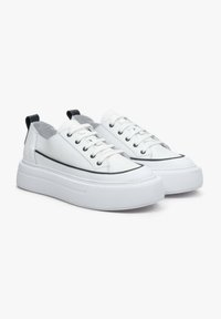 Białe skórzane sneakersy z okrągłym noskiem, teksturowanymi podeszwami, czarnymi akcentami i sznurowanym zapięciem. Posiadają niską cholewkę i pętelkę na pięcie.