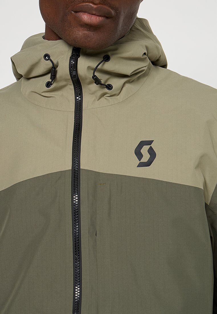 Chaqueta con capucha para hombre en verde oliva y beige. Presenta una tela texturizada, cierre de cremallera, cordones ajustables y un logo en el pecho.