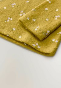 Tessuto giallo con superficie texturizzata, caratterizzato da piccoli motivi floreali bianchi e rosa. Due pezzi piegati si sovrappongono in un angolo.