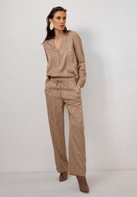 Beige Zweiteiler, bestehend aus einem strukturierten, langärmeligen Oberteil mit V-Ausschnitt und einer lockeren Hose mit elastischem Bund und Kordelzug.