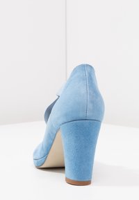 Chaussure à talon haut en suède bleu clair avec un bout rond et un talon épais, présentant une texture lisse et une subtile variation de couleur.