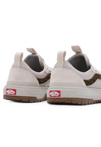 Zapatillas beige claro con material de ante y malla, rayas de acento marrón, suela de goma y un prominente logo rojo de Vans en el talón.