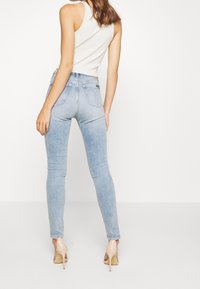 Ljusblå skinny jeans med hög midja, med en blekt tvätt, bakfickor och minimal sömnadsdetaljer. Matchas med beige klackar.