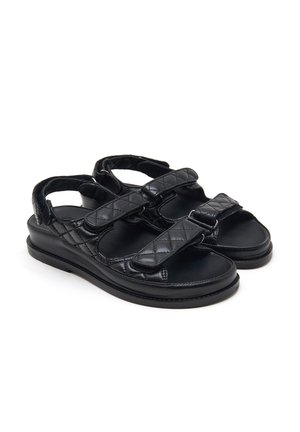 Sandales en cuir noir avec brides matelassées et fermetures Velcro réglables, dotées d'une semelle plate et d'un design à bout ouvert.