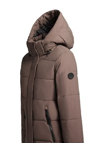 Puffervest i lysebrun, med lynlåslukning foran, stor hætte, sorte detaljer og synligt quiltet mønster. Har sidelommer med lynlås.