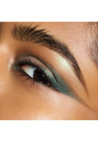 Nærbilde av et øye med grønn og bronse øyenskygge, blandet med en glitrende finish. Definert bryn, mørke vipper og jevn hudtekstur.