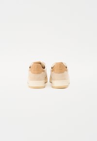 Beige Wildledersneaker mit einer glatten, hellbraunen Leder-Schaftlasche und einer weißen Zunge. Verfügt über eine Gummisohle mit strukturierten Grip-Mustern.