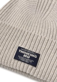 Lys grå ribbet strikhue med et marineblåt mærke, der står "THINKING MU" samt yderligere små hvide tekster.