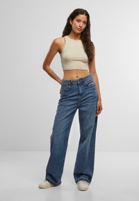Beige crop top and wide-leg blue denim jeans. The jeans have a high waistband with a frayed hem and are paired with light sneakers.