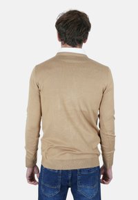 Maglione beige con scollo rotondo e maniche lunghe, realizzato in tessuto a maglia. Indossato con jeans blu, che mostrano una texture liscia e un design aderente.