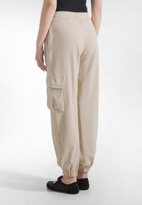 Beżowe, luźne spodnie cargo z elastycznymi mankietami i sznurkiem w pasie. Posiadają boczne kieszenie i miękką, teksturowaną tkaninę.