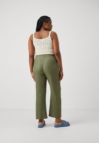 Crochet tank top in off-white, textured olive green wide-leg pants, and blue slip-on sandals. Showcases layered textures and colors.