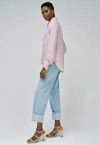 Camisa de manga larga color rosa claro con un corte relajado y puños atados, combinada con unos pantalones vaqueros de mezclilla sueltos y de color azul claro, y sandalias de tacón alto color marrón.