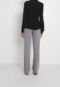 Černý top s dlouhým rukávem s nařasenými detaily na zádech, doplněný šedými rozšířenými kalhotami z měkké látky, které poskytují pohodlný střih.