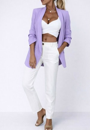 Femme portant un blazer lilas, un crop top blanc, un pantalon blanc taille haute, des talons beiges et des colliers en or superposés sur fond blanc.