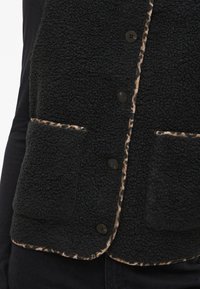 Black fleece vest with leopard print trim, five black buttons, and two front pockets. Features a soft, textured surface and relaxed fit.