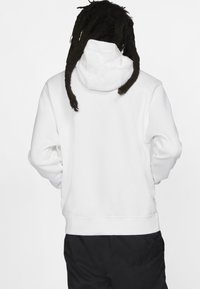 Sweatshirt à capuche blanche avec une texture en polaire, présentant une poche kangourou et des poignets côtelés, vu de l'arrière.